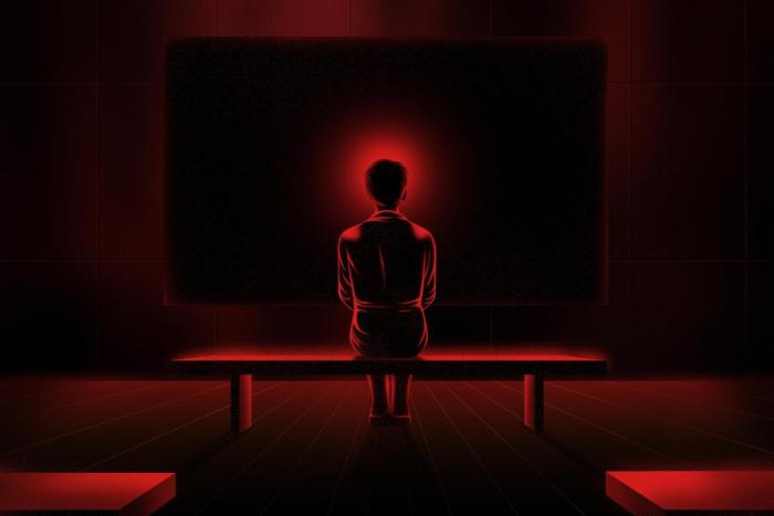 The back of a female figure sitting on a bench, with a red halo around her head, against a background of a dark projection screen.