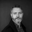 head and shoulders portrait of man with beard wearing a cardigan